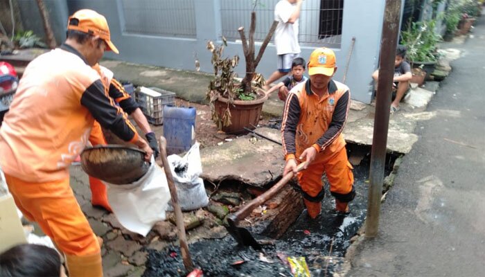 Petugas PPSU sedang membersihkan saluran penuh lumpur. (wandi)