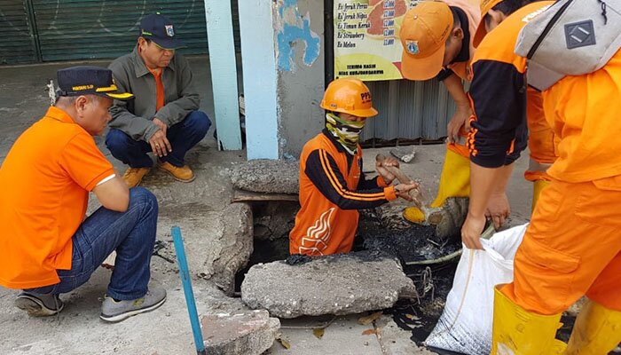 Petugas sedang membersihkan saluran air yang penuh lumpur dan sampah. (wandi)